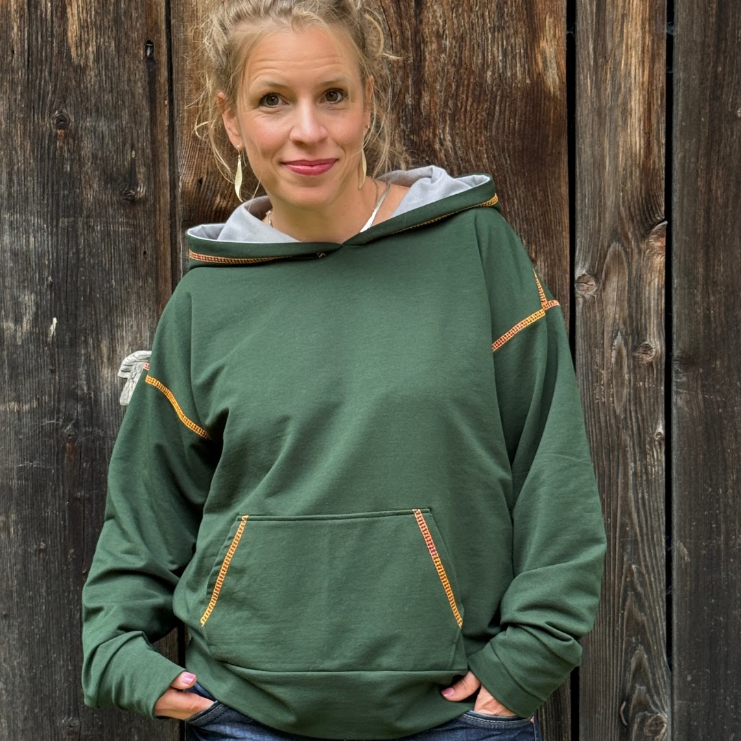 Claudia Witticke im selbst gen&auml;hten gr&uuml;nen Hoodie vor einer Holzwand